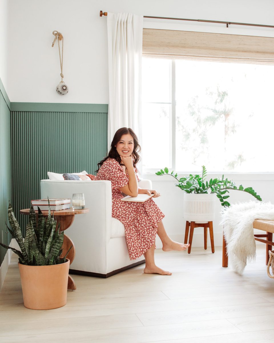 Anita sits in a white upholstered chair against a green paneled wall