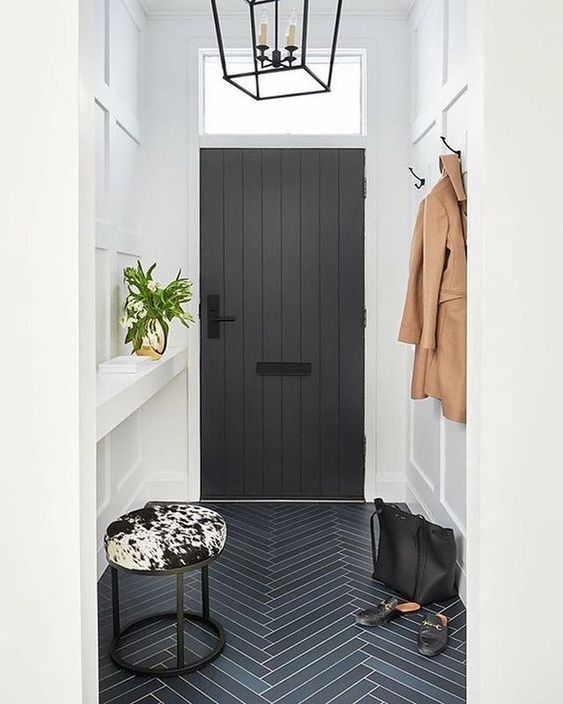 High-ceilinged entry with white walls, black herringbone tiles, and cowhide stool