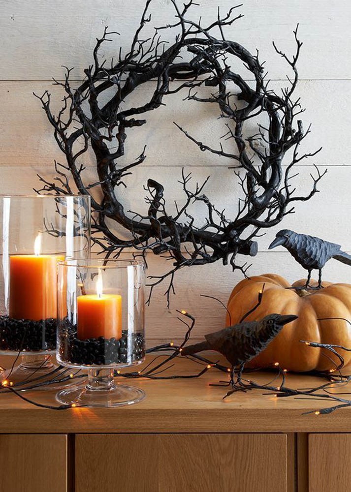 a black wreath of gnarled branches set above orange candles and a pumpkin staged with crow statues