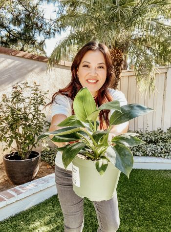 Anita in the backyard, holding out a plant