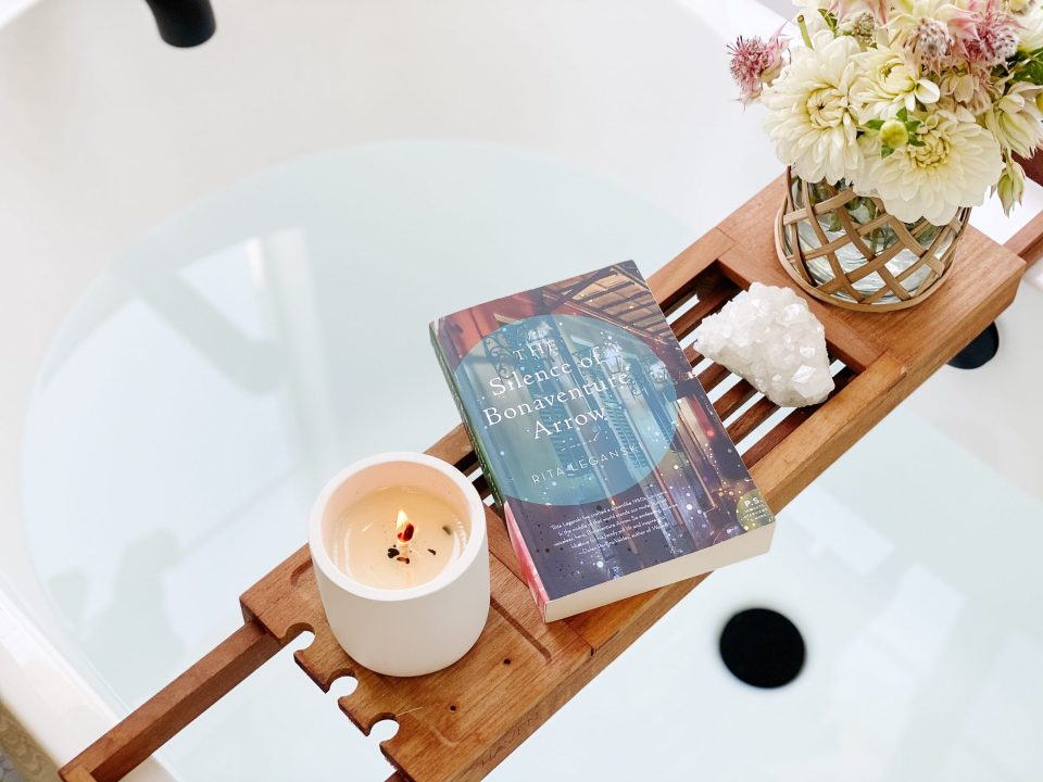 A candle burning on the bathtub caddy beside a vase of flowers
