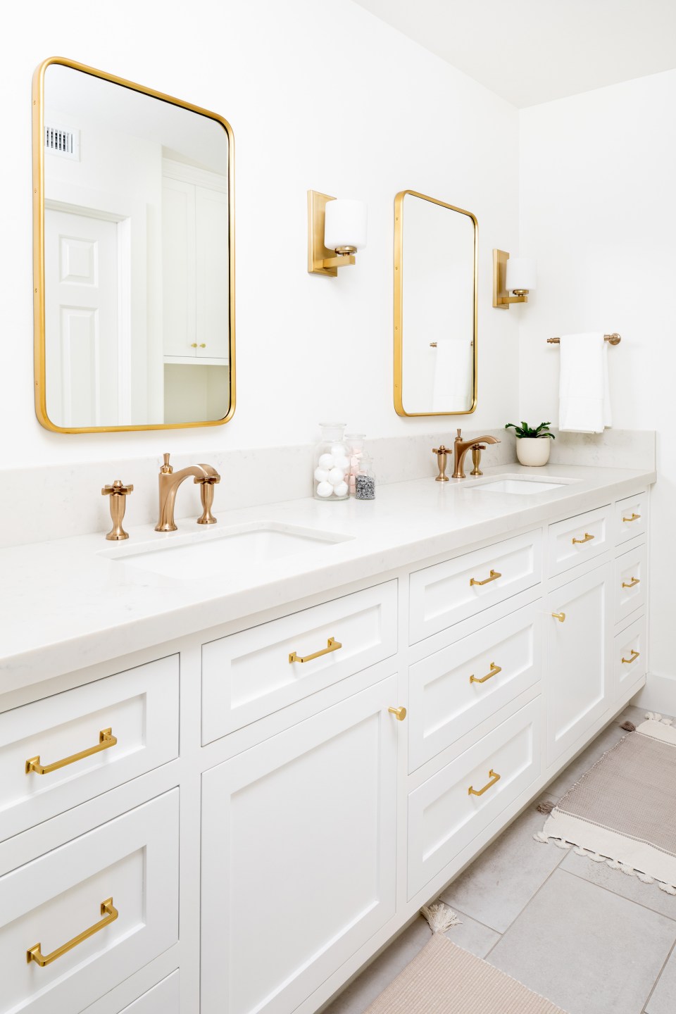 Bright white cabinets and countertops are accented by brass faucets, fixtures, sconces, and mirrors